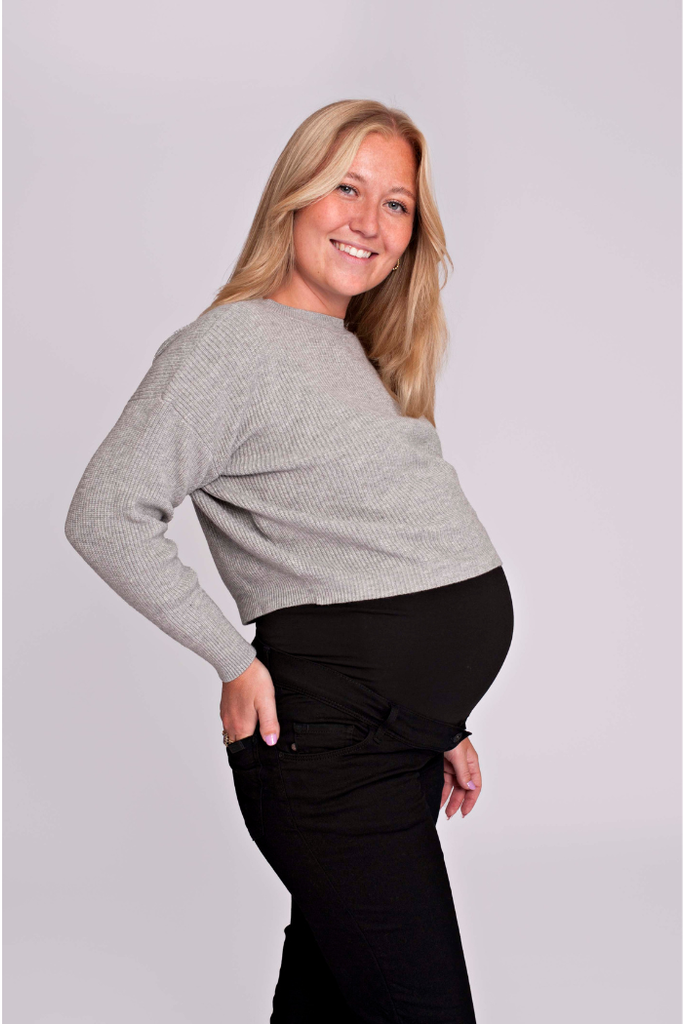 Femme enceinte portant un pull cropped gris lumineux, vue de profil en studio | mummy nantes